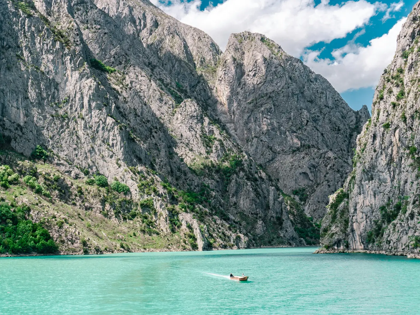 Two sea kayaks on the flat green water of Komani Lake beneath high canyon walls