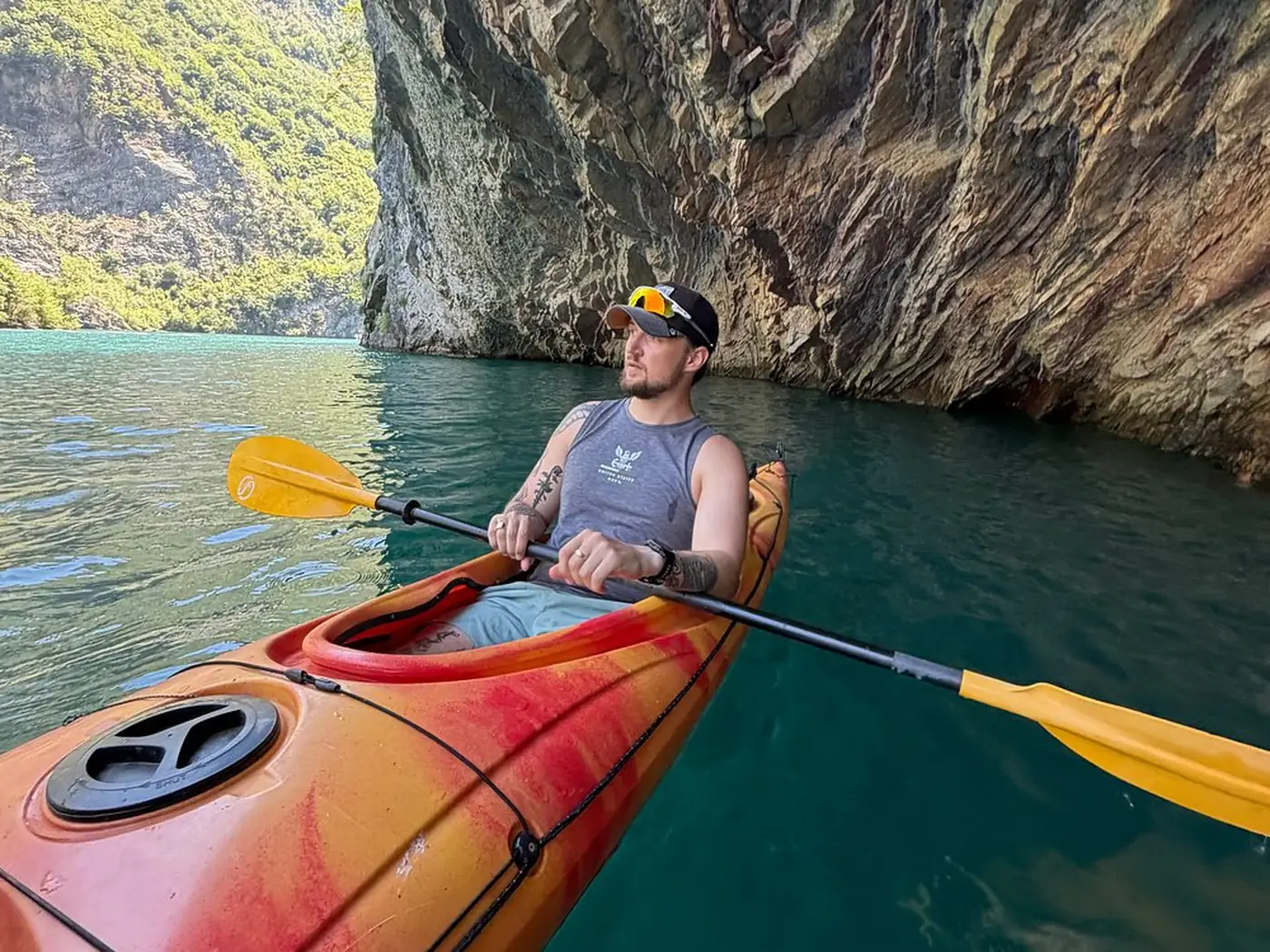 Two sea kayaks on the flat green water of Komani Lake beneath high canyon walls